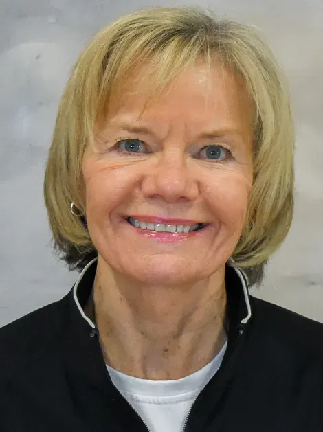 Smiling woman with short blonde hair in a black jacket against a light gray background