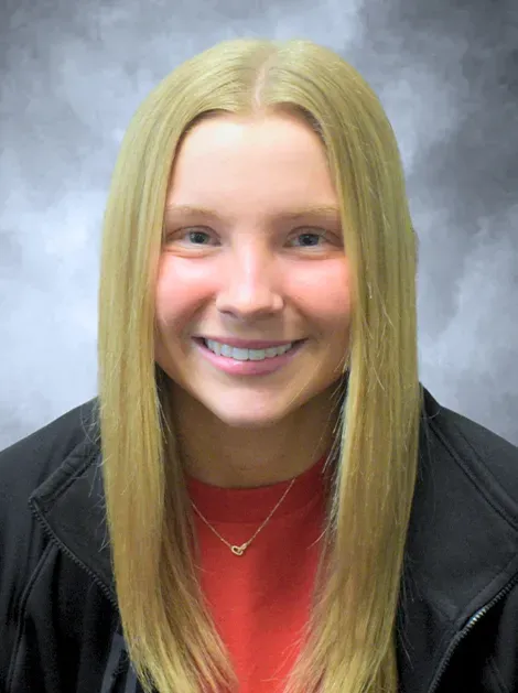 Smiling person in a red shirt and black jacket against a gray backdrop