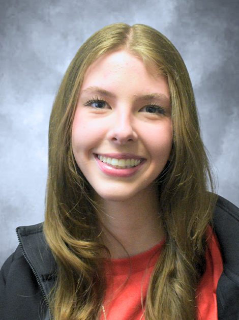 Smiling person with long light brown hair in a red shirt against a gray backdrop