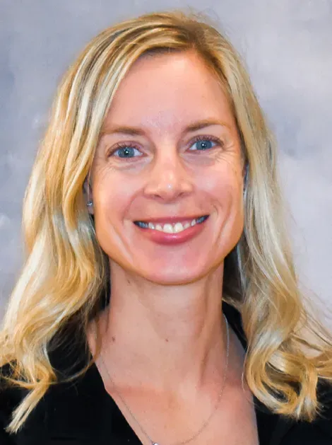 Smiling blonde woman in a black top against a light gray background