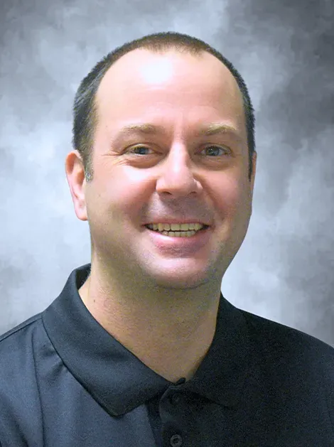 Smiling man in a dark polo shirt against a soft gray background
