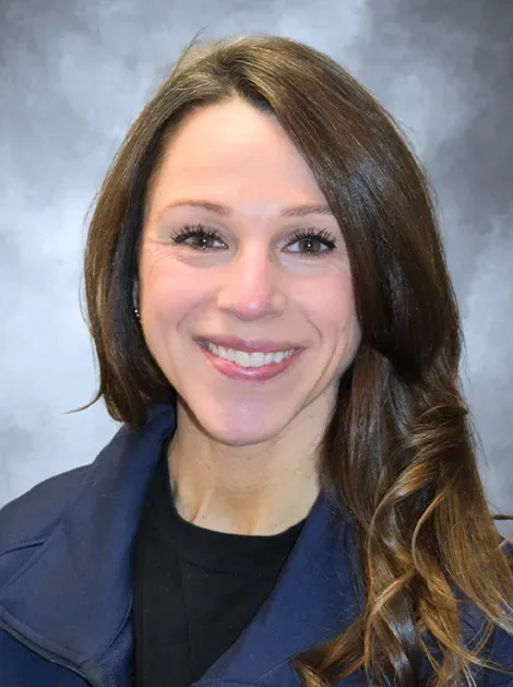 Smiling woman in a navy jacket against a gray studio backdrop