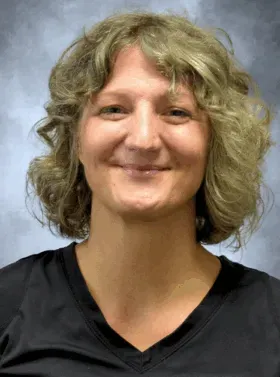 Smiling person with curly blonde hair wearing a black shirt against a gray backdrop