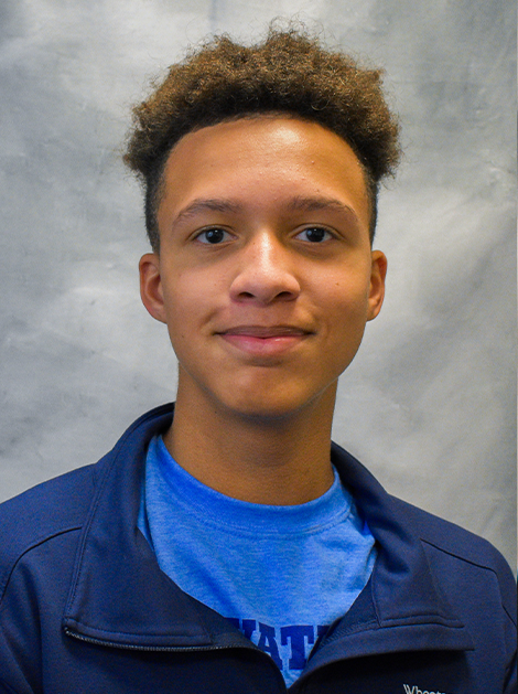 Portrait of a person in a blue jacket and shirt against a gray background, smiling slightly
