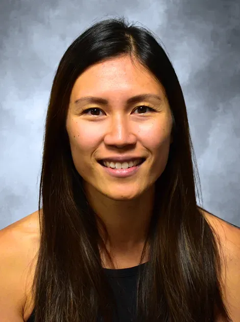 Smiling woman with long dark hair against a gray studio backdrop