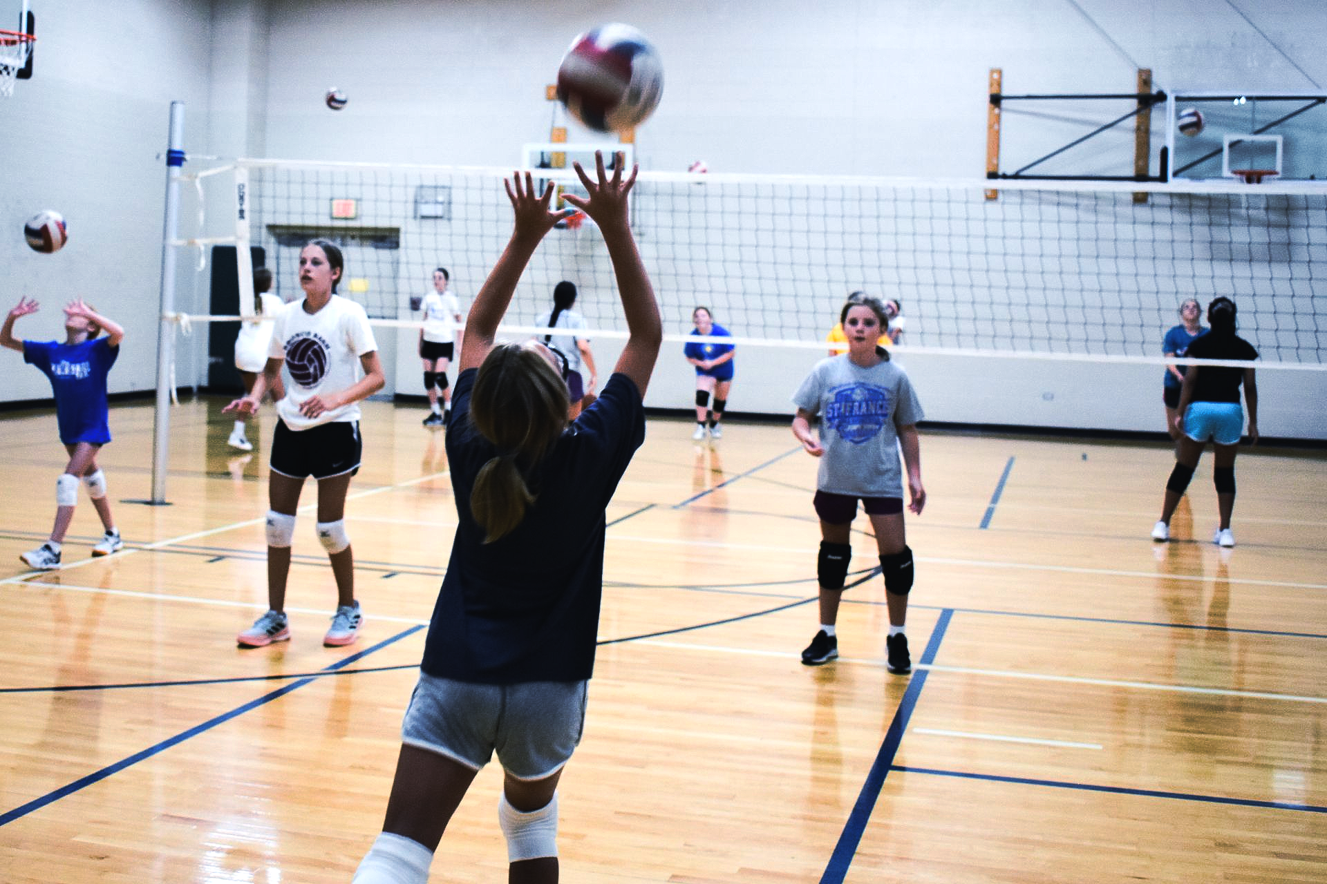 Indoor volleyball practice with players on a gym court, one reaching up to set the ball
