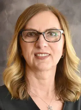 Portrait of a woman with glasses and shoulder-length blonde hair against a gray background