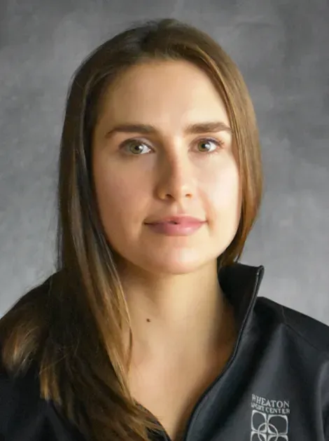 Portrait of a woman with long brown hair, wearing a black jacket, against a gray background