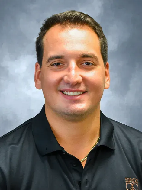 Smiling man in a black polo shirt against a gray studio backdrop