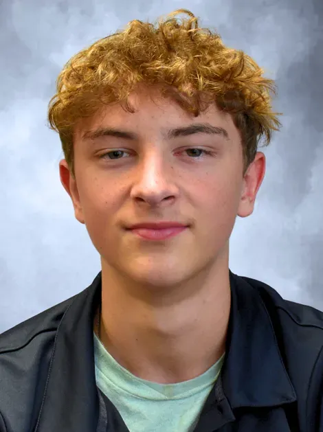 Portrait of a smiling person with curly blond hair against a blue-gray backdrop