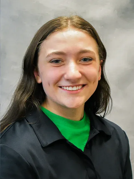 Smiling person in a black jacket over a bright green shirt against a gray backdrop