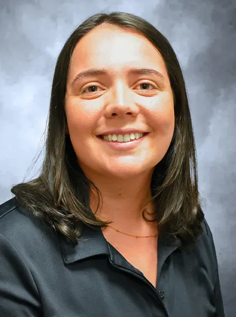 Headshot of a smiling person with dark hair wearing a black collared shirt against a gray background