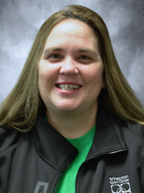 Smiling woman in a black jacket and green shirt against a gray studio backdrop