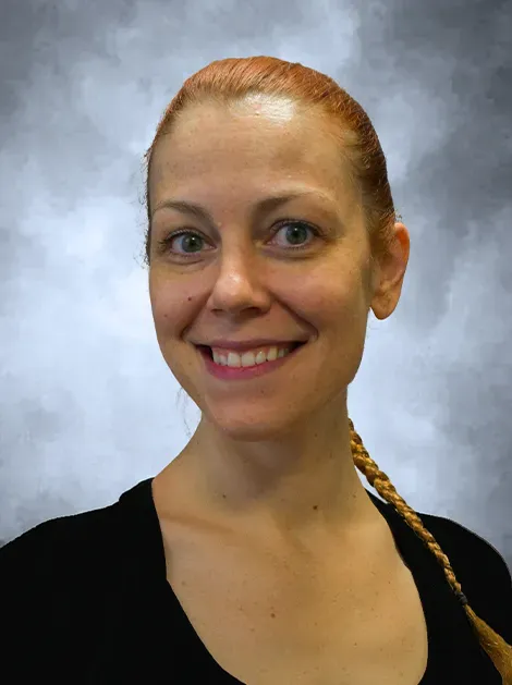 Smiling woman with red hair in a braid against a gray studio background