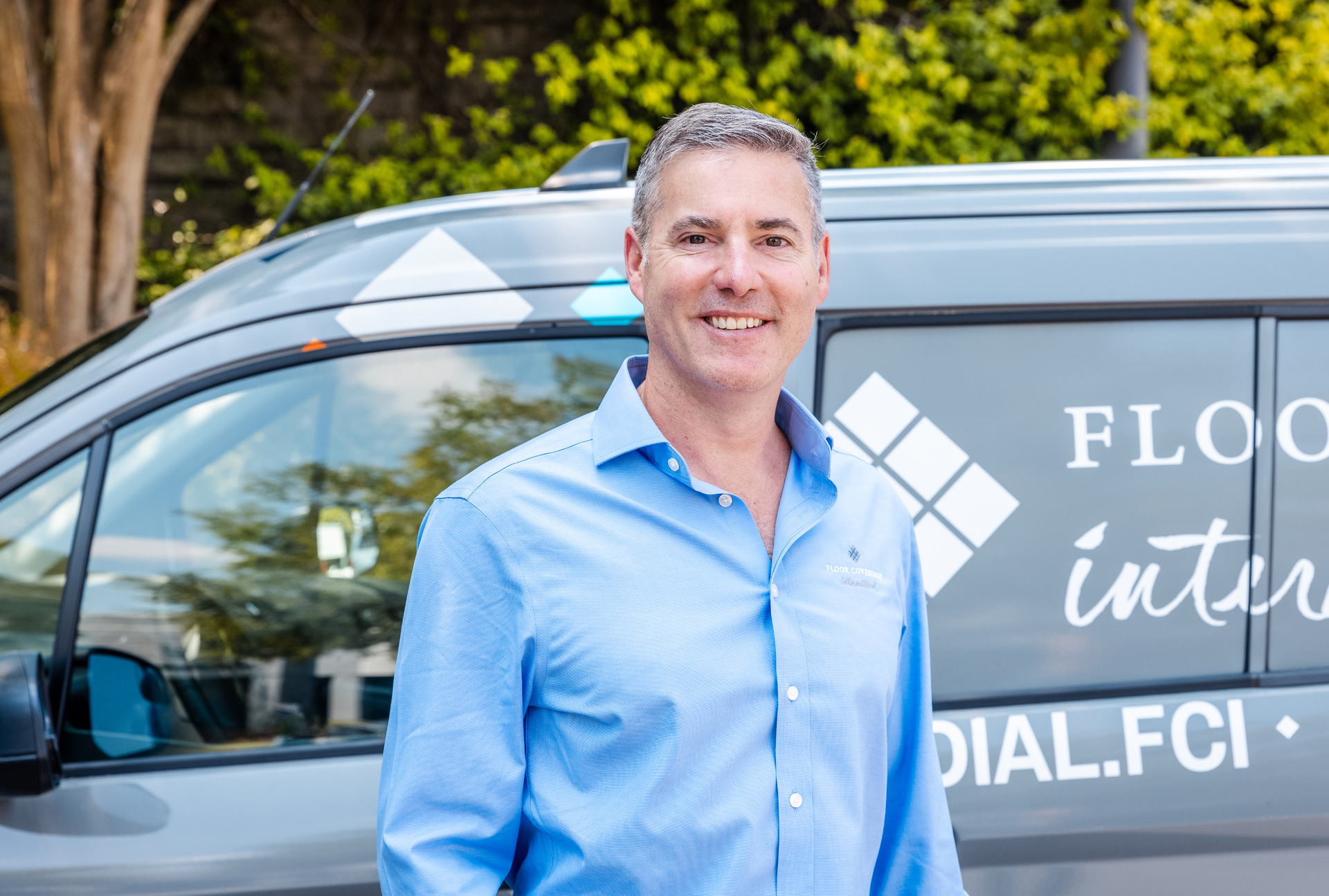 Smiling man in a blue shirt standing beside a branded van outdoors