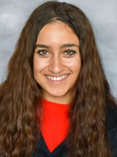 Smiling person with long wavy hair wearing a red top against a gray background