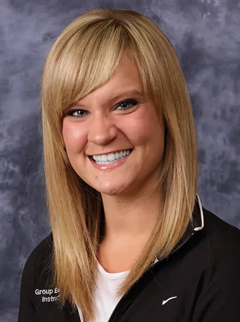 Smiling woman with blonde hair in a black jacket against a gray backdrop