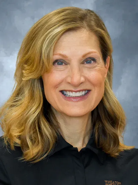 Smiling woman with blonde hair in a black shirt against a gray background