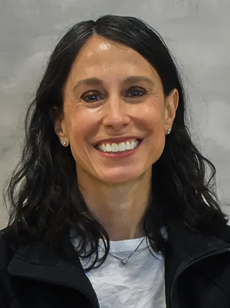 Smiling woman with dark hair wearing a black jacket against a gray background