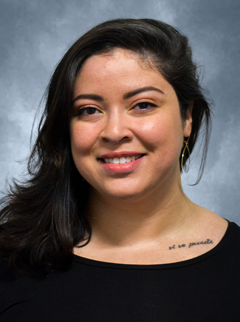 Portrait of a smiling person with dark hair in a black top against a gray studio backdrop
