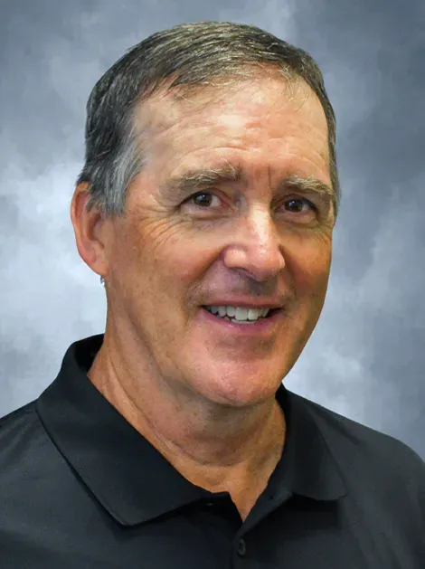 Portrait of a smiling man in a black polo shirt against a blue-gray background