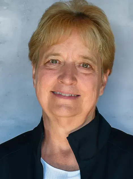 Portrait of a smiling person against a blue background, wearing a dark jacket.