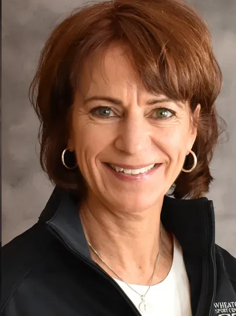 Smiling woman in a black jacket and hoop earrings against a neutral studio background