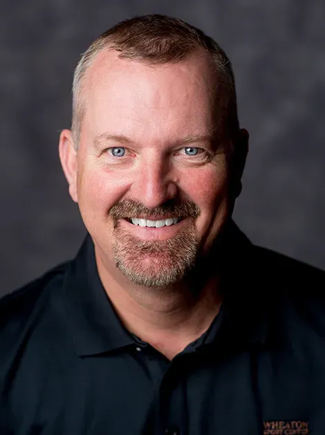 Smiling man in a dark polo shirt against a gray studio backdrop