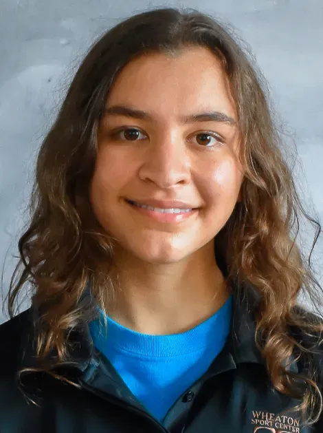 Person smiling in a black jacket and blue shirt against a gray background