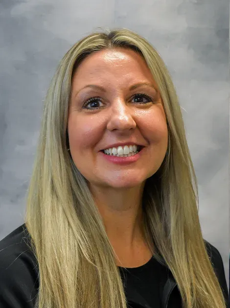 Smiling blonde woman in a black top against a gray studio backdrop