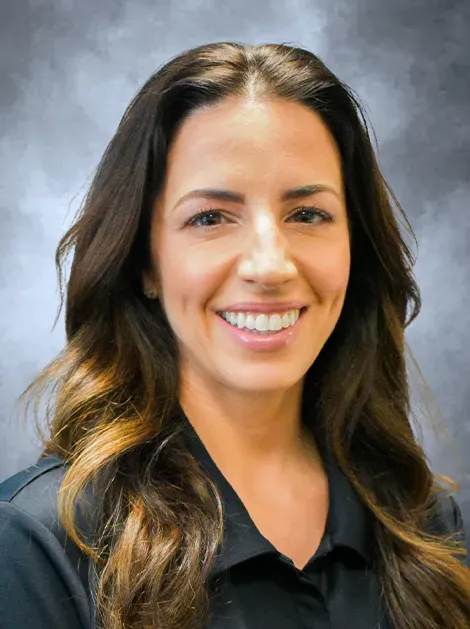 Portrait of a smiling person with long dark hair in a black shirt against a gray studio background