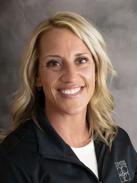 Smiling blonde woman in a dark jacket against a gray studio backdrop