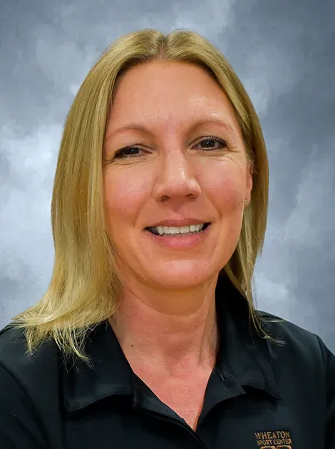 Smiling blonde woman in a black polo shirt against a gray studio backdrop