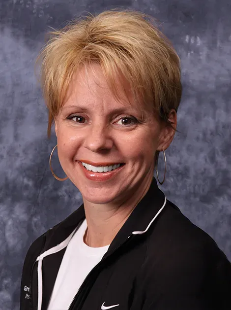 Smiling woman in a black jacket against a gray studio backdrop