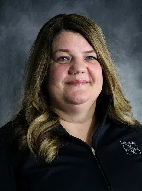 Portrait of a smiling woman in a black zip-up top against a dark studio background