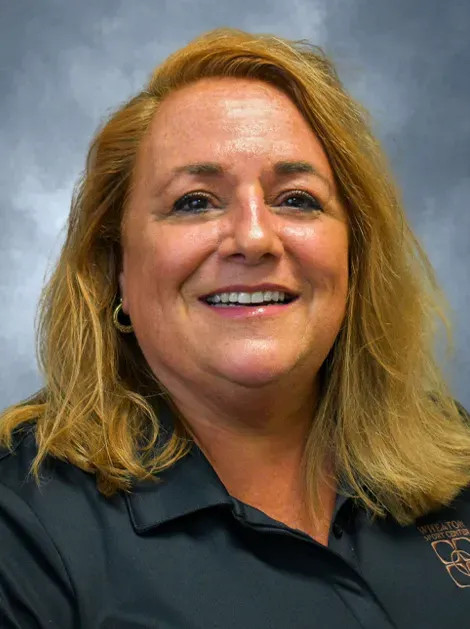 Smiling woman with blonde hair wearing a dark polo shirt against a gray background