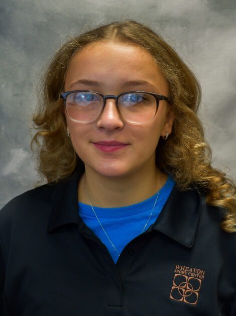 Person wearing glasses and a dark polo shirt against a gray studio backdrop.