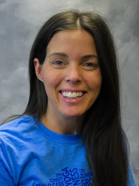 Smiling person with long dark hair in a blue shirt against a gray background