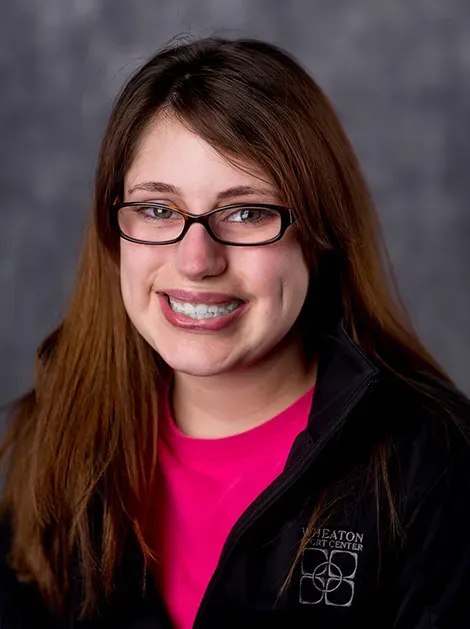 Portrait of a smiling person with glasses wearing a black jacket over a bright pink shirt