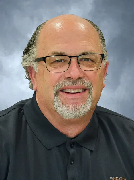 Smiling man with glasses and goatee in a dark polo shirt against a gray studio backdrop