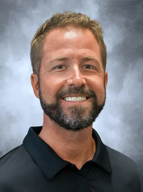 Smiling man with short hair and beard in a black polo against a gray studio backdrop