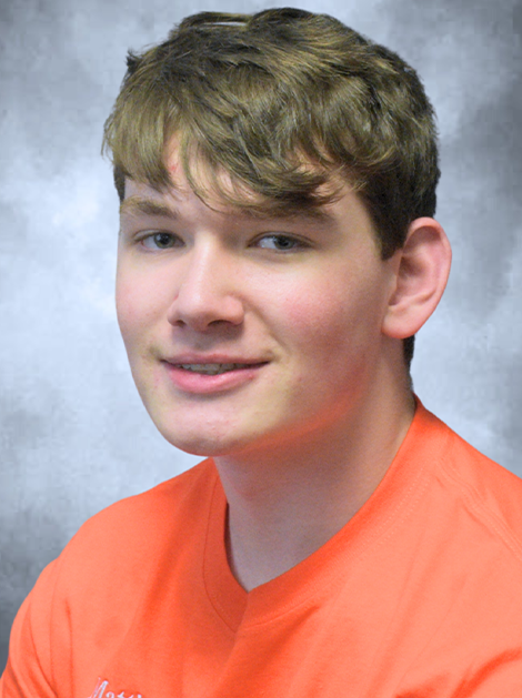 Young person in an orange shirt smiling against a gray studio backdrop