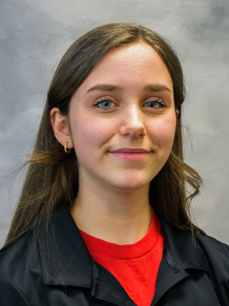 Portrait of a smiling person in a black jacket over a red shirt against a gray backdrop
