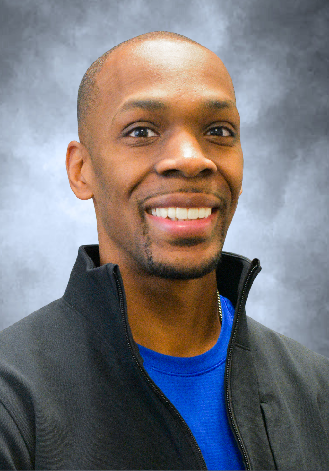 Smiling man in a black jacket over a blue shirt against a gray background