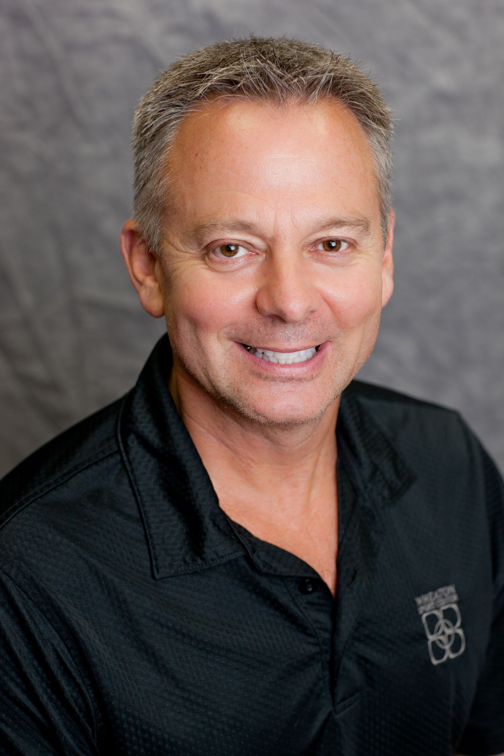 Smiling man in a black polo shirt against a gray studio backdrop