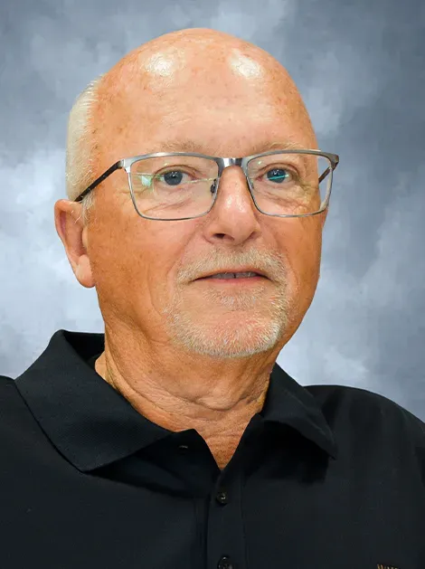 Portrait of a man wearing glasses and a black polo shirt against a gray-blue backdrop