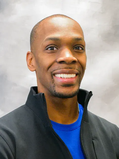 Smiling man in a black jacket and blue shirt against a gray background