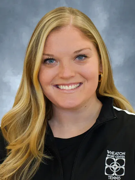 Smiling blonde woman in a black jacket against a blue-gray studio backdrop