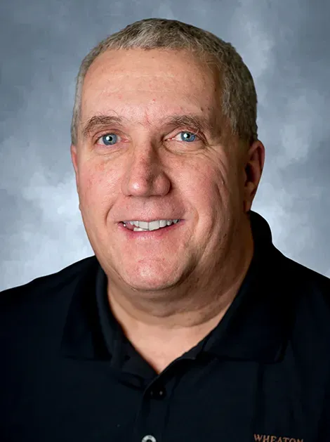 Smiling man in a black polo shirt against a gray studio background