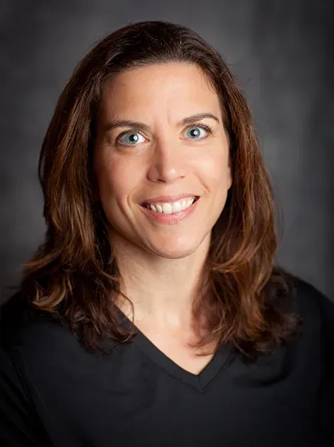 Smiling woman with shoulder-length brown hair against a dark background